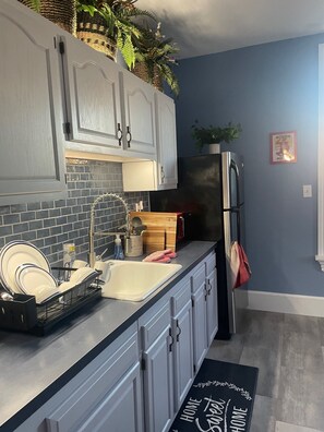 Een keuken met grijze kastjes, een roestvrijstalen koelkast, een wastafel met een moderne kraan, en een bordenrek met borden.