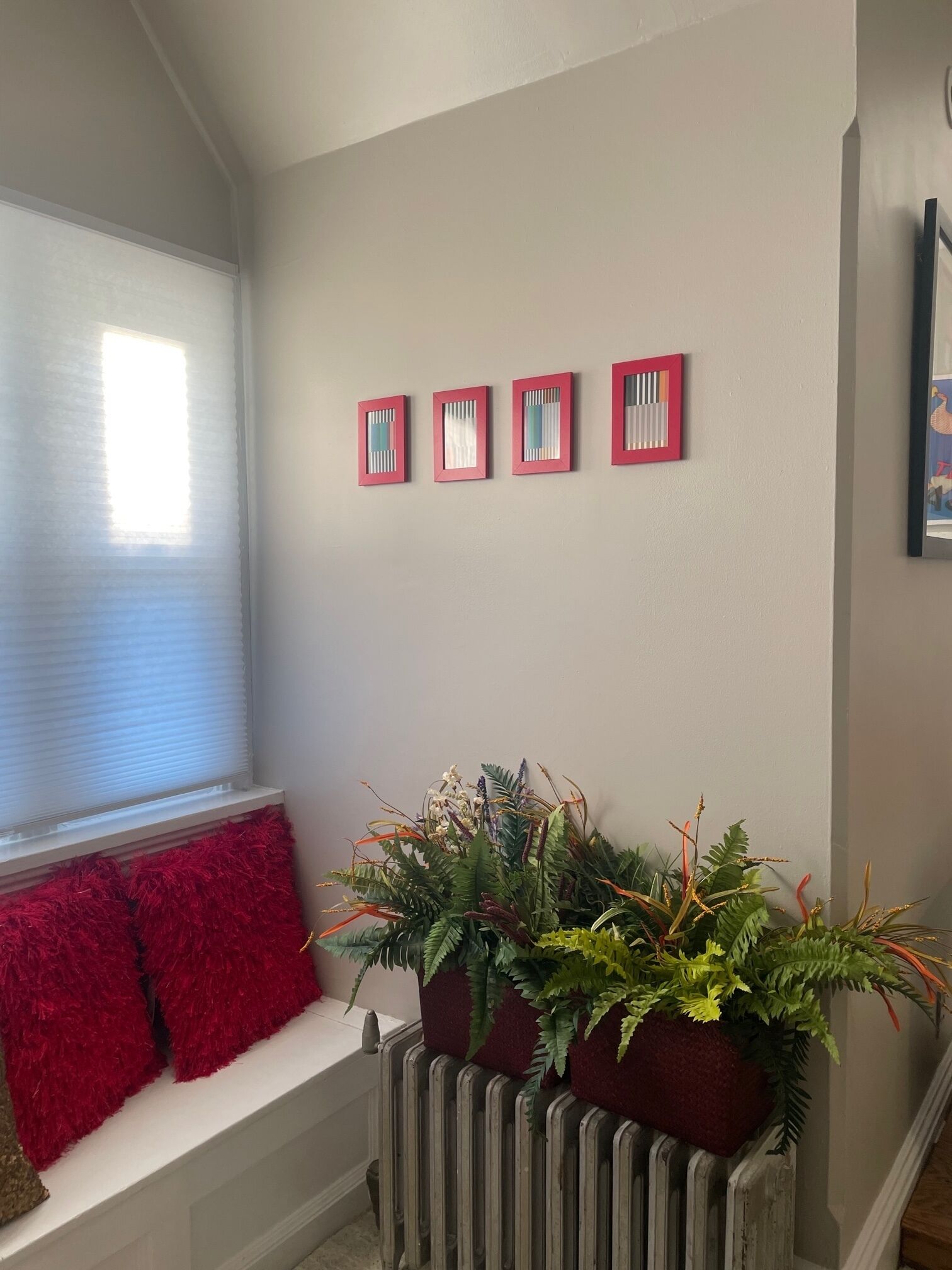 A room with a window, a bench with red cushions, and three square wall decorations.