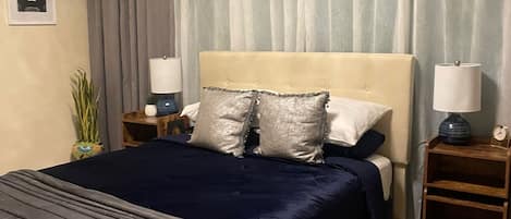 Un dormitorio con una cama, dos mesitas de noche, una lámpara y un cuadro colgado en la pared.