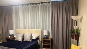 Una camera da letto con un letto, due comodini, una lampada, una panca e tende.