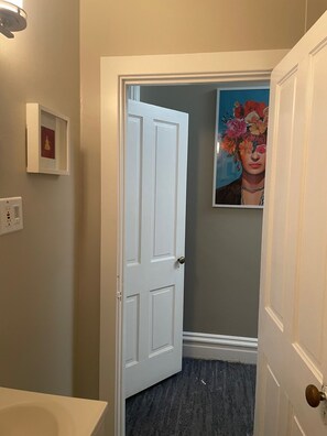 A hallway with a white door, a framed picture on the wall, and a light fixture above the door.