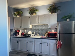 A kitchen with grey cabinets, a stainless steel refrigerator, a red toaster, and a microwave.
