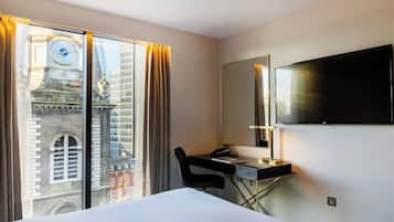 A hotel room with a bed, a desk, a chair, a TV, and a large window with curtains.