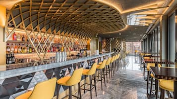 A bar area with a curved ceiling, a long counter with bottles, and yellow bar stools.