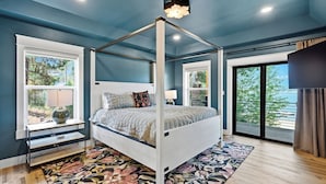 Ein Schlafzimmer mit einem Himmelbett, großen Fenstern, Blick ins Freie und einer Deckenleuchte.