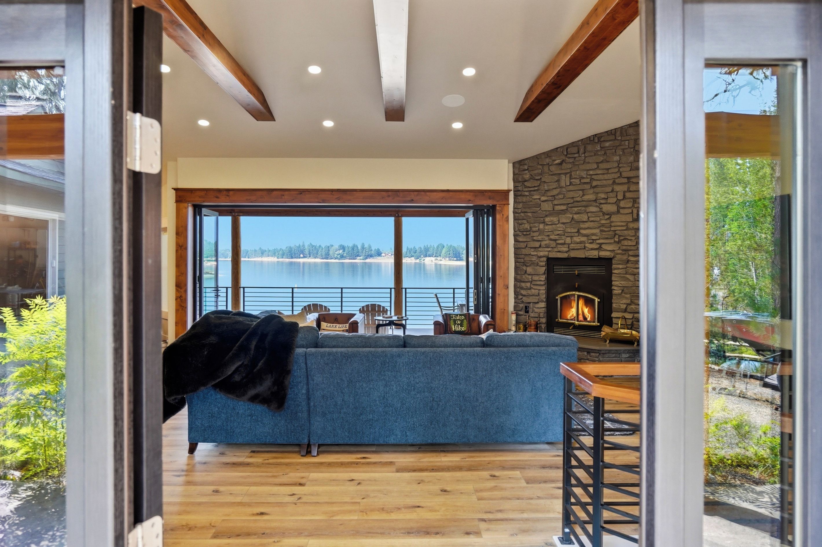 A modern living room with a stone fireplace, a large window overlooking a body of water, and a cozy seating area.