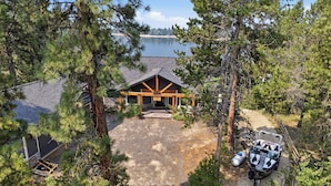 Ein Chalet mit überdachter Veranda, einer Schotterauffahrt und einem Boot, das vor der Tür liegt.
