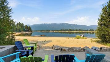 Un espacio de descanso junto al lago con sillas Adirondack y un pozo de fuego, con vistas a un lago tranquilo y montañas lejanas.