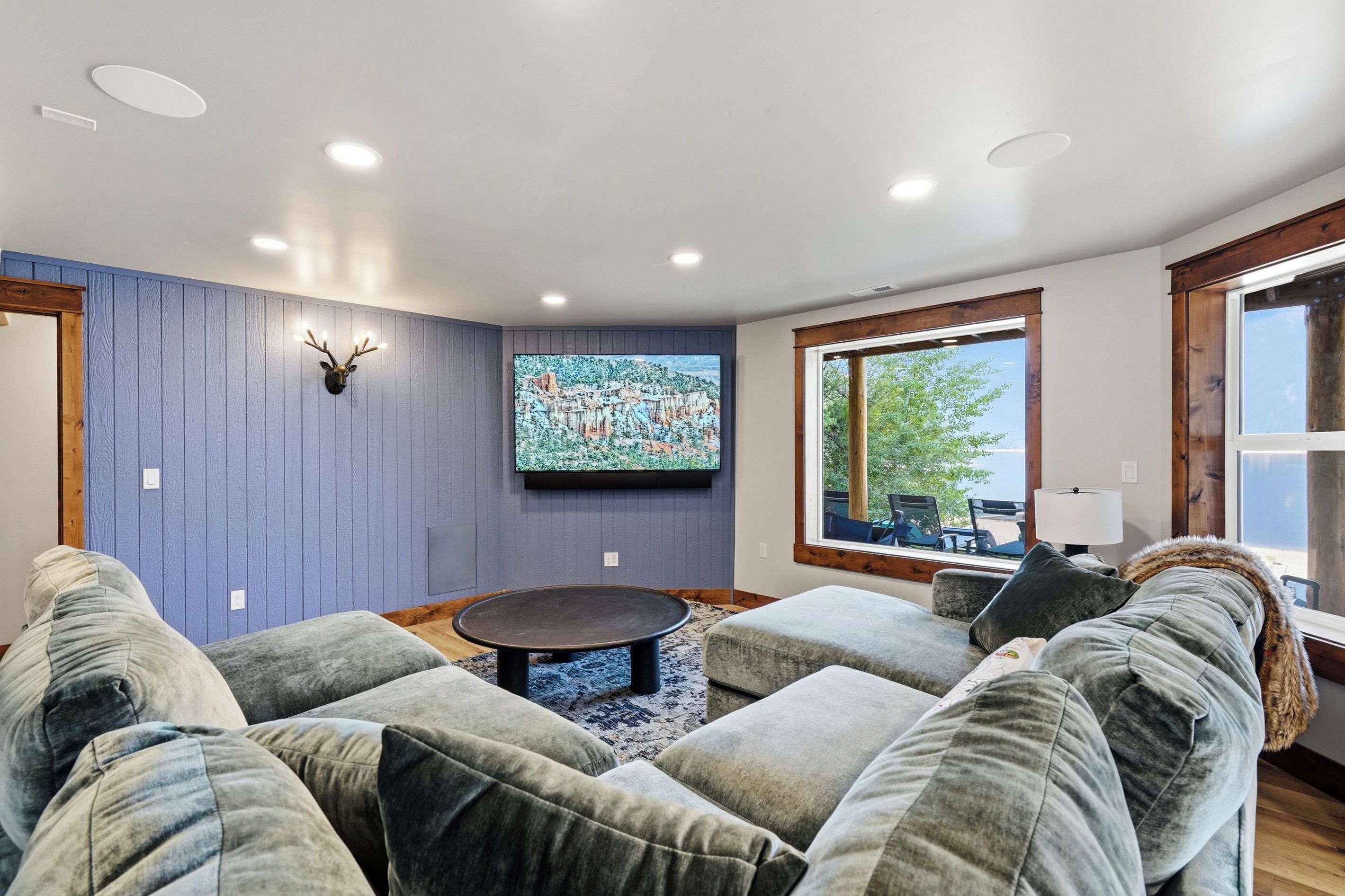 Una sala de estar con un televisor montado, una cabeza de venado decorativa y un ventanal con vistas al exterior.