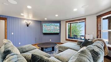 Una sala de estar con un televisor montado, una cabeza de venado decorativa y un ventanal con vistas al exterior.