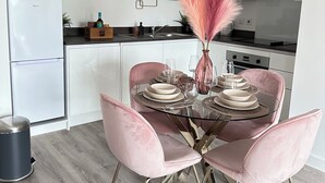 Una cocina moderna con armarios blancos, una mesa de comedor preparada para cuatro personas y un florero decorativo con plumas rosas.