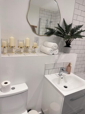 A bathroom with a toilet, sink, and a mirror. There are candles on a stand, a potted plant, and rolled towels on the counter. - Stylish Central Derby 2 Bed, 2 Bath | Free Parking, Gym & Near Station (Derby)