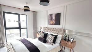 Un dormitorio moderno con una cama grande, una mesita de noche, una lámpara de pie y una ventana con cortinas.
