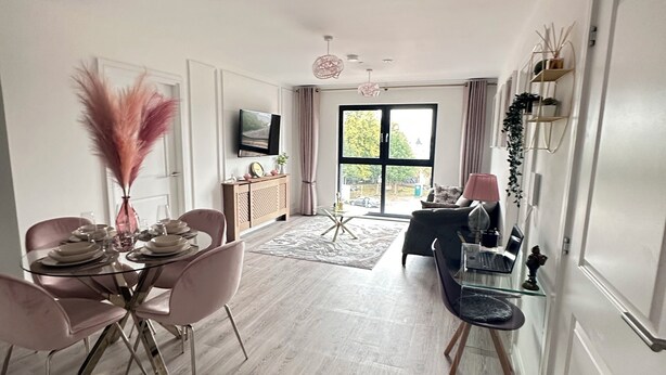 Un espacio de estar moderno con comedor, zona de descanso con sofá y mesa de centro, y televisor montado en la pared.