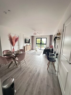 A modern living space with a dining area, a seating area with a sofa and a coffee table, and a television mounted on the wall. - Stylish Central Derby 2 Bed, 2 Bath | Free Parking, Gym & Near Station (Derby)