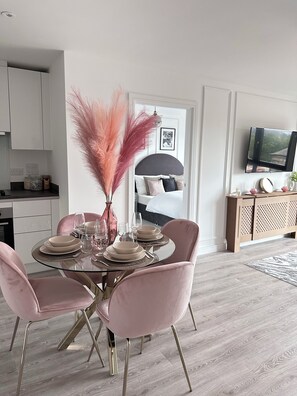 A dining area with a round table, pink chairs, and a vase with pink feathers. - Stylish Central Derby 2 Bed, 2 Bath | Free Parking, Gym & Near Station (Derby)