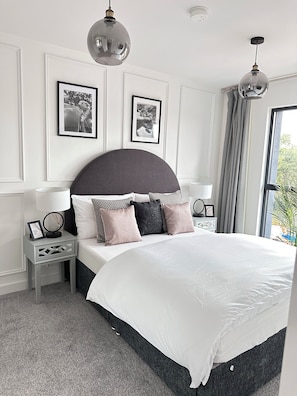 A modern bedroom with a large bed, two bedside tables, a mirror, and framed pictures on the wall. - Stylish Central Derby 2 Bed, 2 Bath | Free Parking, Gym & Near Station (Derby)