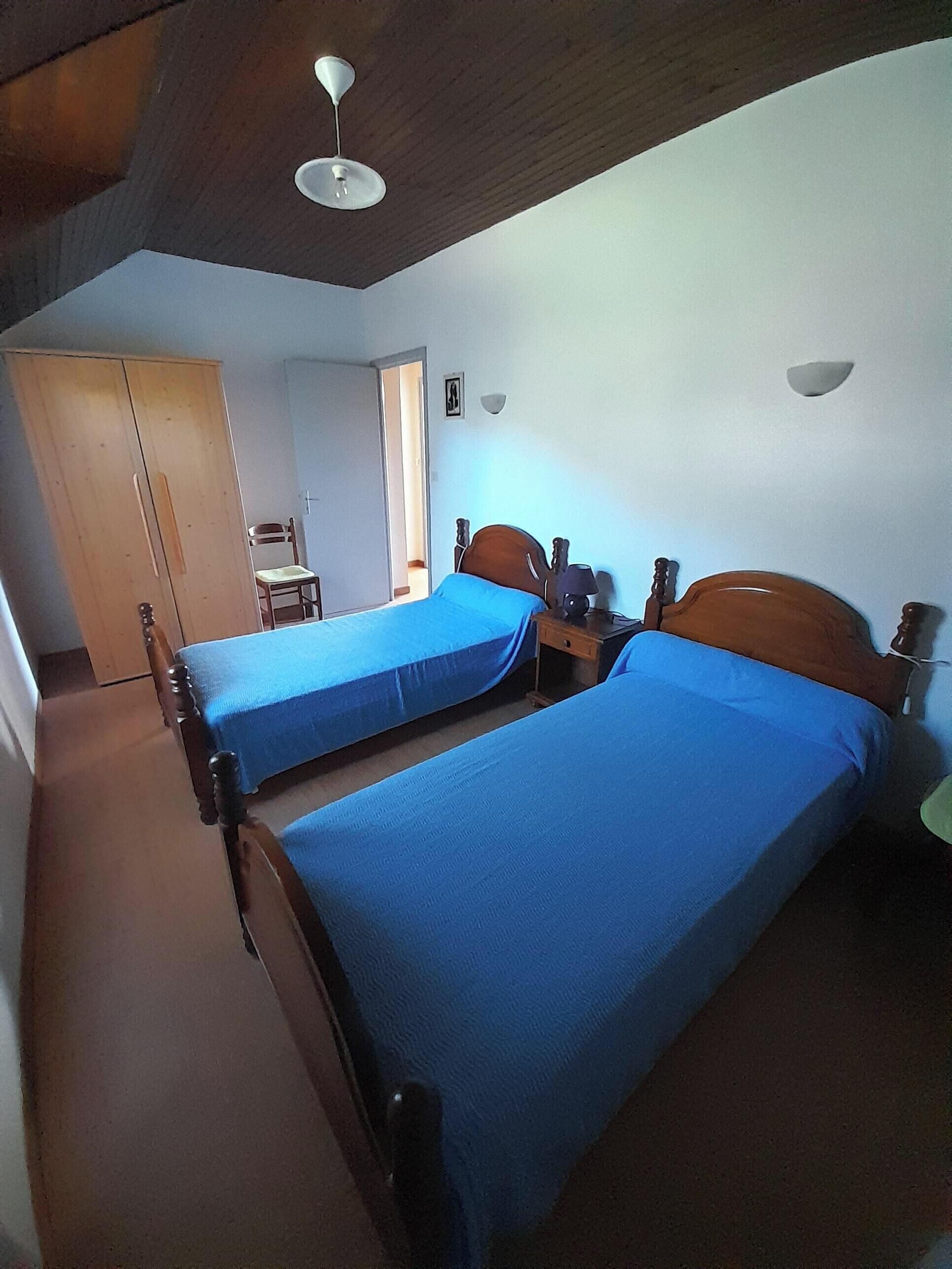 Een kamer met twee enkele bedden, een houten garderobe, een stoel en een plafondventilator.