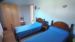 A room with two single beds, a wooden wardrobe, a chair, and a ceiling fan.
