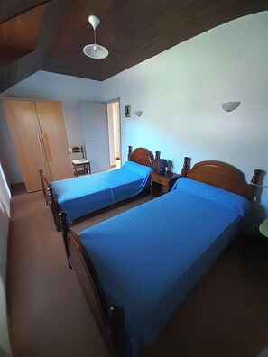 Ein Zimmer mit zwei Einzelbetten, einem Holzschrank, einem Stuhl und einem Deckenventilator.