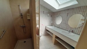 A bathroom with a skylight, a shower, and two sinks with mirrors.