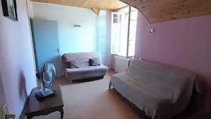 A bedroom with a bed, a sofa, a small table, and a fan.