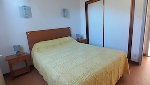 A bedroom with a bed, bedside table, wall-mounted light, and a sliding door.