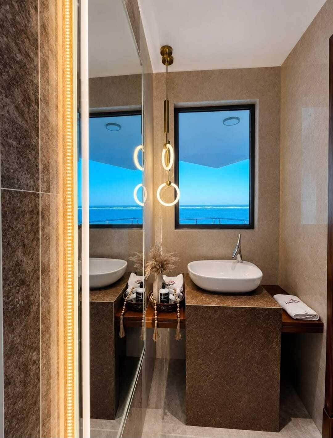Un baño moderno con dos lavamanos, un espejo grande y vista al océano.