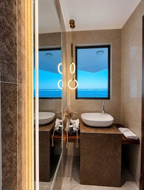 Un baño moderno con dos lavamanos, un espejo grande y vista al océano.