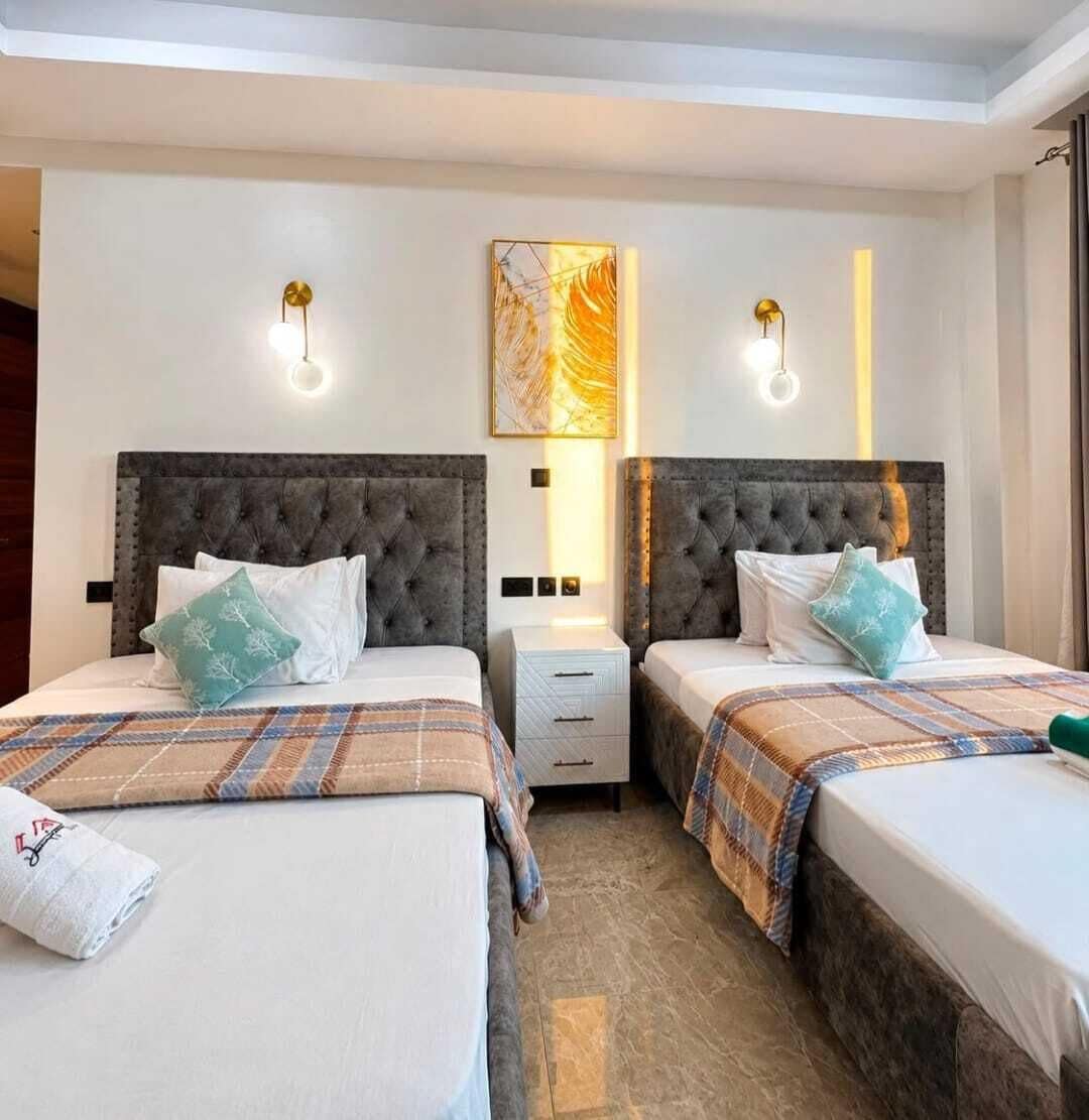 Habitación de hotel con dos camas, una mesita de noche, una obra de arte en la pared y apliques.