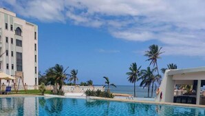 A swimming pool with a tiled deck, palm trees, and a building in the background. - Comforts Seaview Apartments-Nyali (Mombasa)