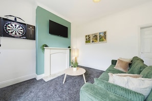 Een woonkamer met een dartbord, een flatscreen televisie, een open haard en een groene bank.
