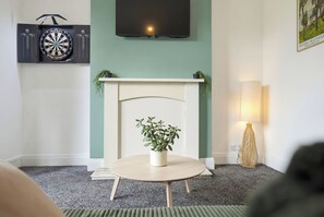Een woonkamer met een open haard, een dartbord, een televisie en een plant.