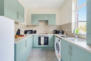 Een compacte keuken met een magnetron, oven en wasmachine, een spoelbak en een raam met uitzicht.