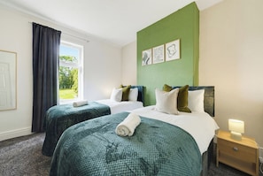 Een hotelkamer met twee bedden, een groene accentmuur en een raam met gordijnen.