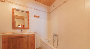 Une salle de bain avec un meuble-lavabo en bois, un miroir, une baignoire et une douche.