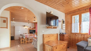 Une pièce chaleureuse avec un plafond en bois, un téléviseur fixé au mur, une table à manger avec des chaises et un canapé.