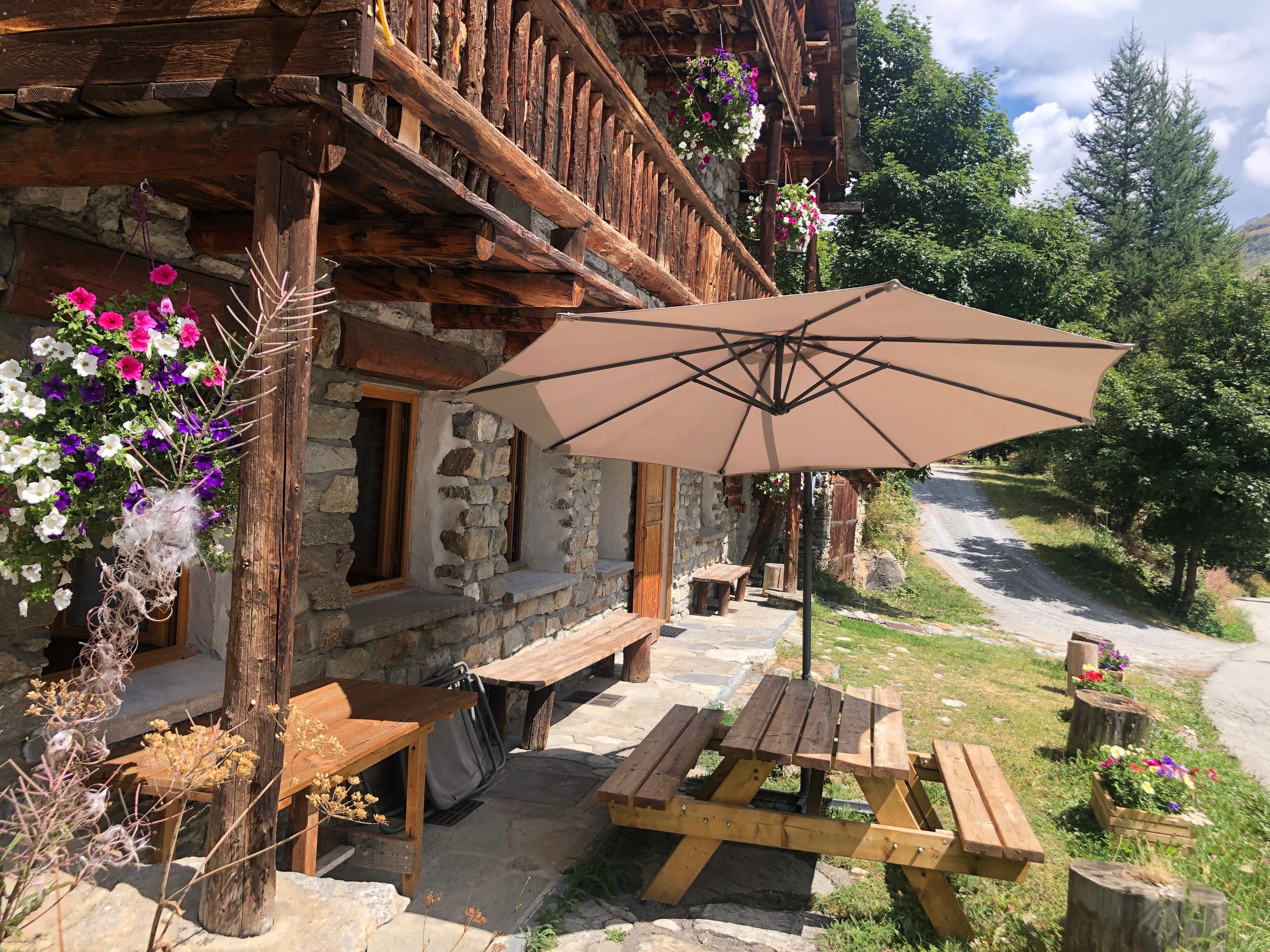Un bâtiment rustique en pierre, doté de balcons en bois, d’un espace extérieur aménagé pour s’asseoir et d’un grand parasol offrant de l’ombre.