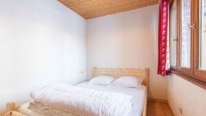 Een slaapkamer met een bed, houten plafond en een raam met gordijnen.