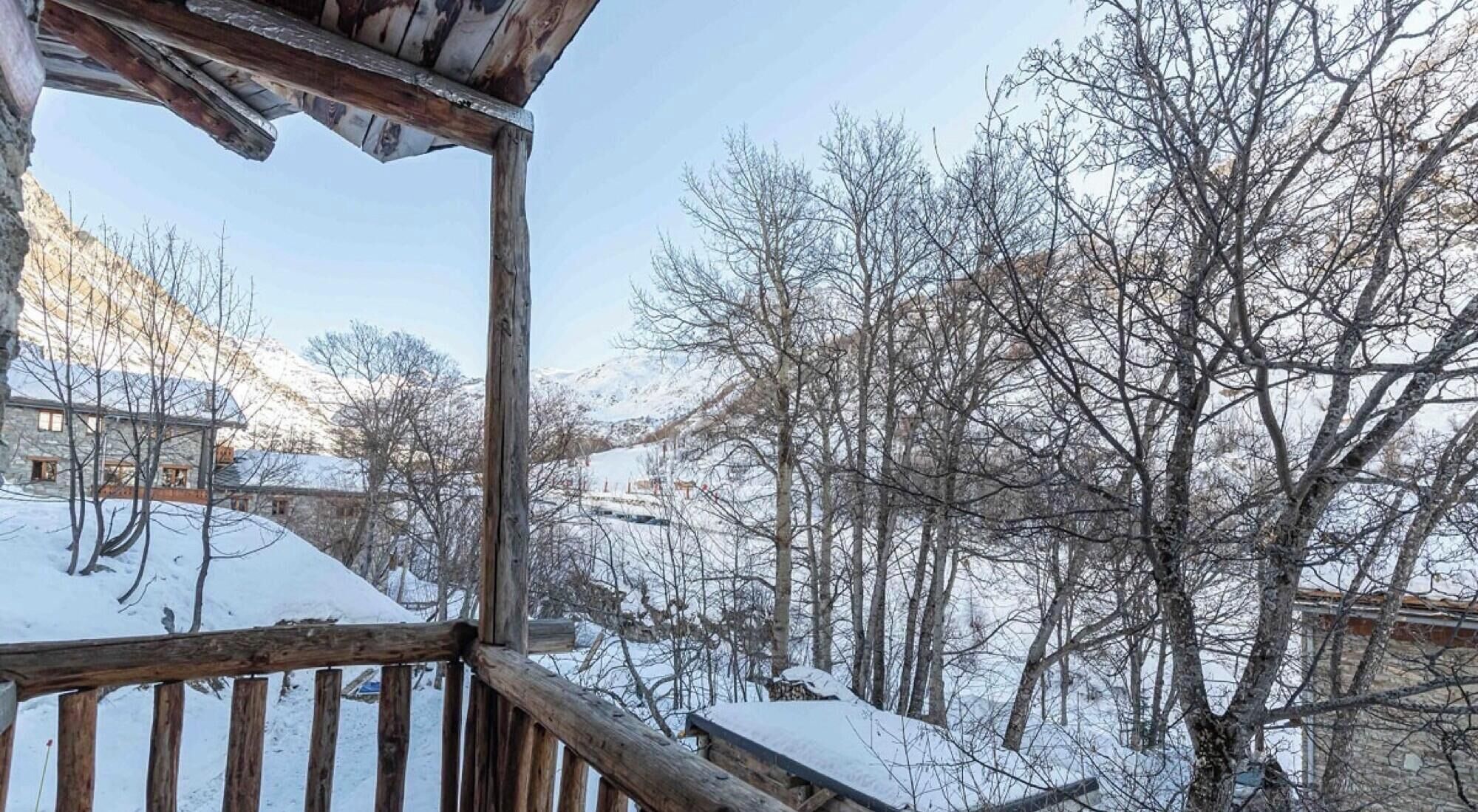 A wooden balcony with a view of snow-covered trees and a stone building in the background.