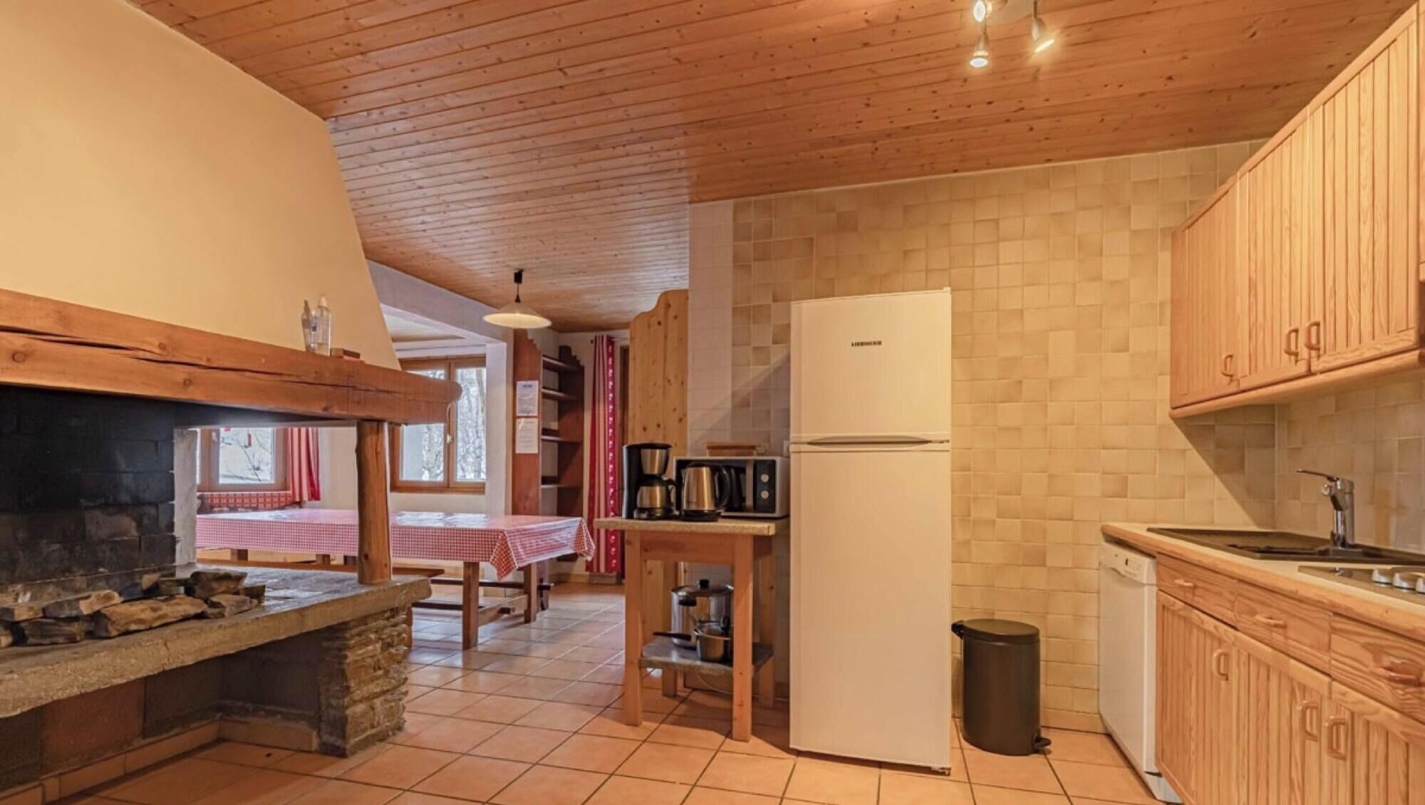 Une cuisine compacte avec une cheminée en pierre, un réfrigérateur blanc, des armoires en bois et un dosseret carrelé.