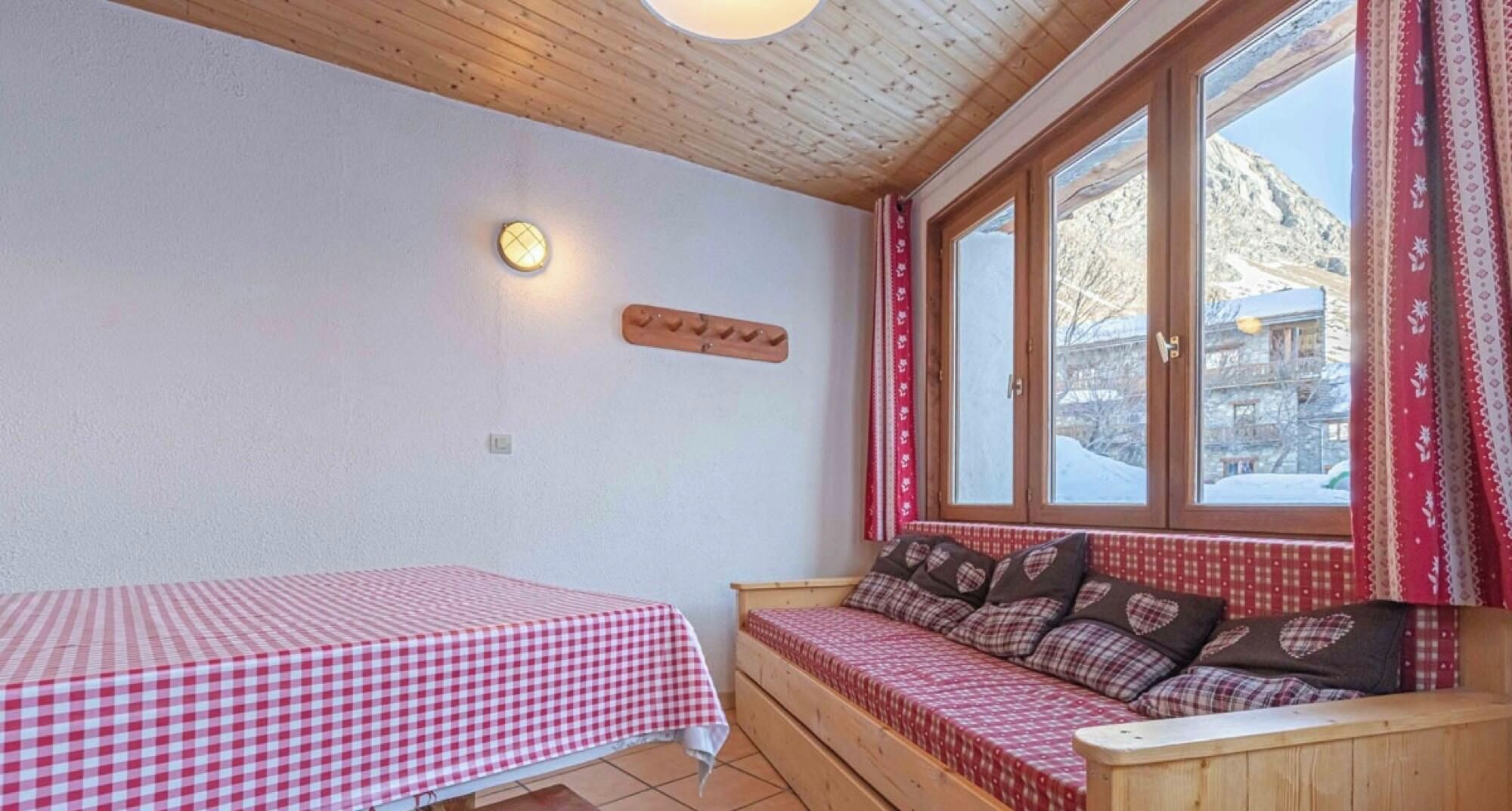 Ett rum med ett rutigt bord, en bänk med kuddar, en vägglampa och ett fönster med gardiner.