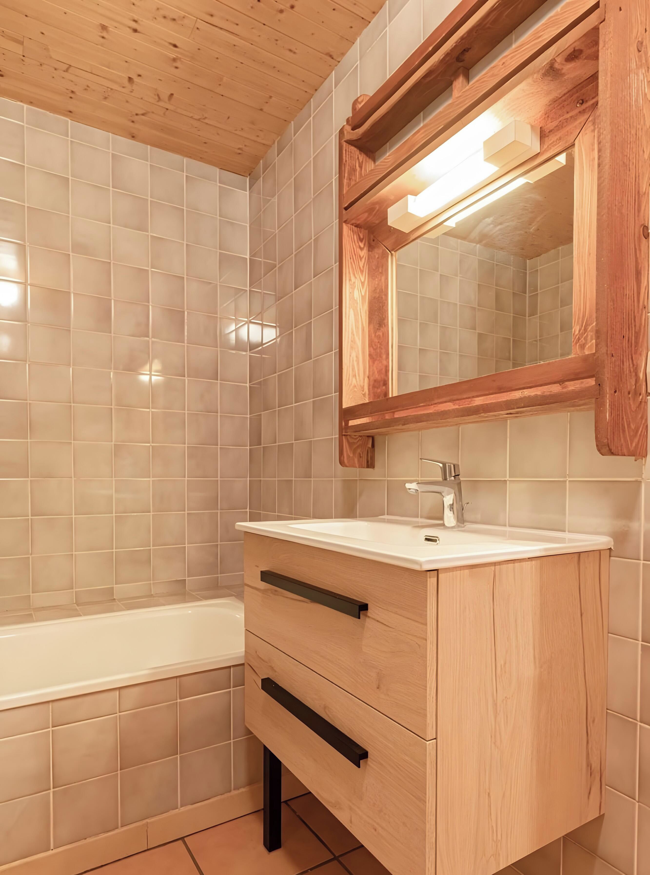 Un baño con tocador de madera, un lavamanos blanco y un espejo.