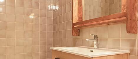 Un baño con tocador de madera, un lavamanos blanco y un espejo.