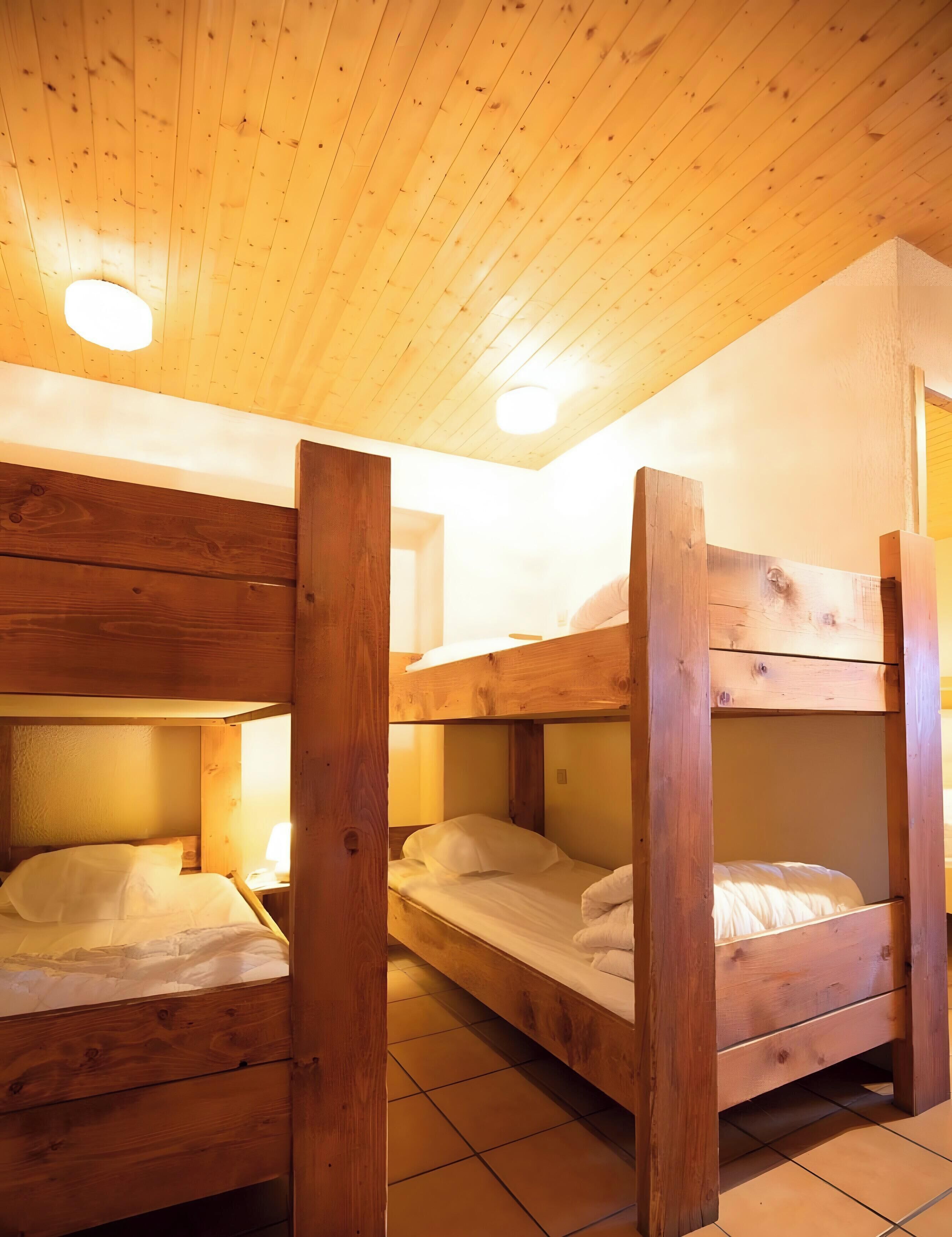 Una stanza con letti a castello in legno, pavimento piastrellato e soffitto con travi in legno e illuminazione a incasso.