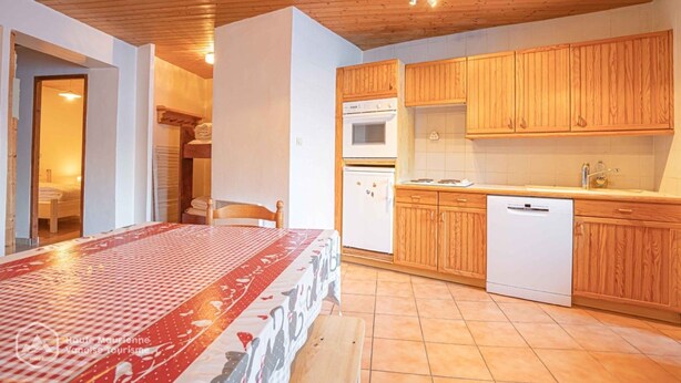 A room with a bed, a wooden ceiling, a kitchen with wooden cabinets, a white refrigerator, and a white dishwasher. - Chalet Grand Sénail 3 — 53m², mountain view, Bonneval (Bonneval-sur-Arc)