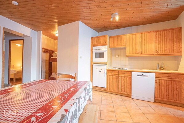 Une pièce comprenant un lit, un plafond en bois, une cuisine avec des meubles en bois, un réfrigérateur blanc et un lave-vaisselle blanc.