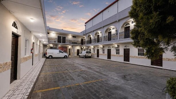 Pátio com chão pavimentado, uma van branca e um edifício com várias varandas e janelas.