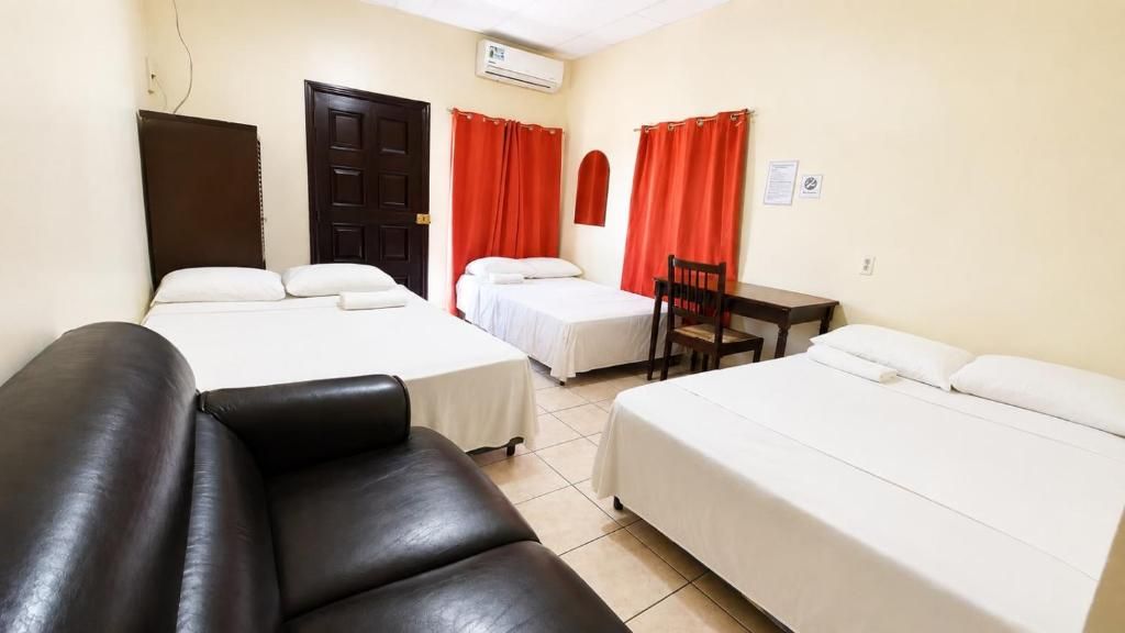 Une chambre d’hôtel avec deux lits, un canapé en cuir noir, une table en bois et des rideaux rouges.
