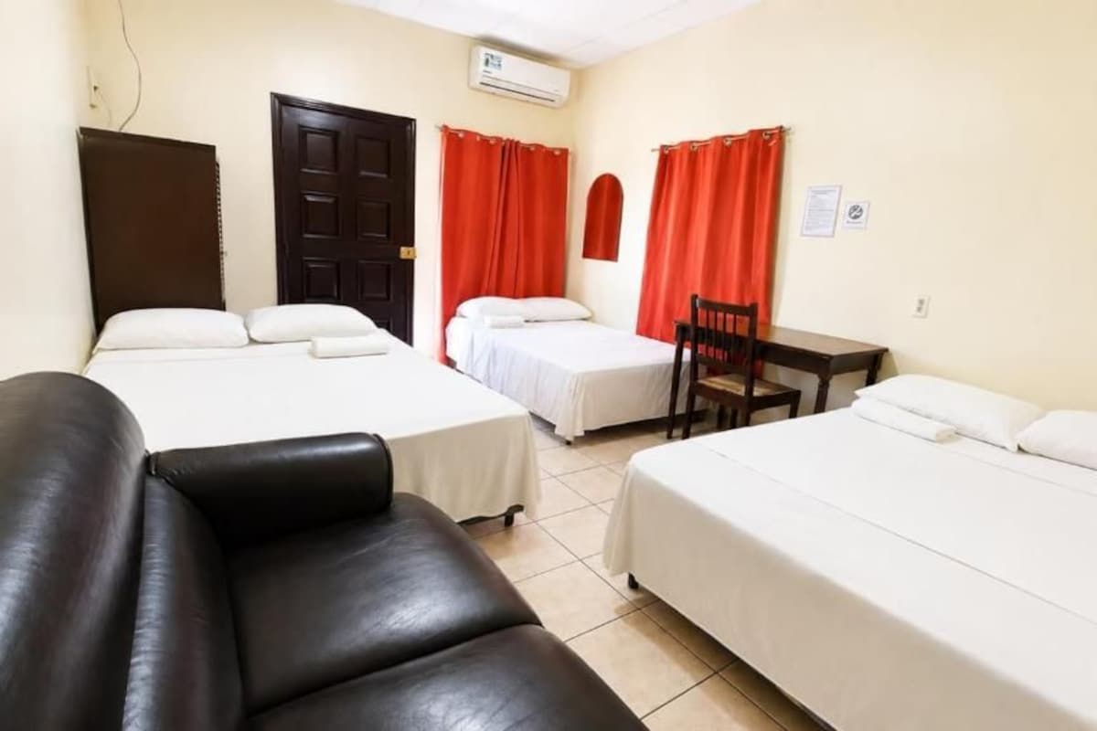 Une chambre d’hôtel avec deux lits, un canapé en cuir noir, une table en bois et des rideaux rouges.